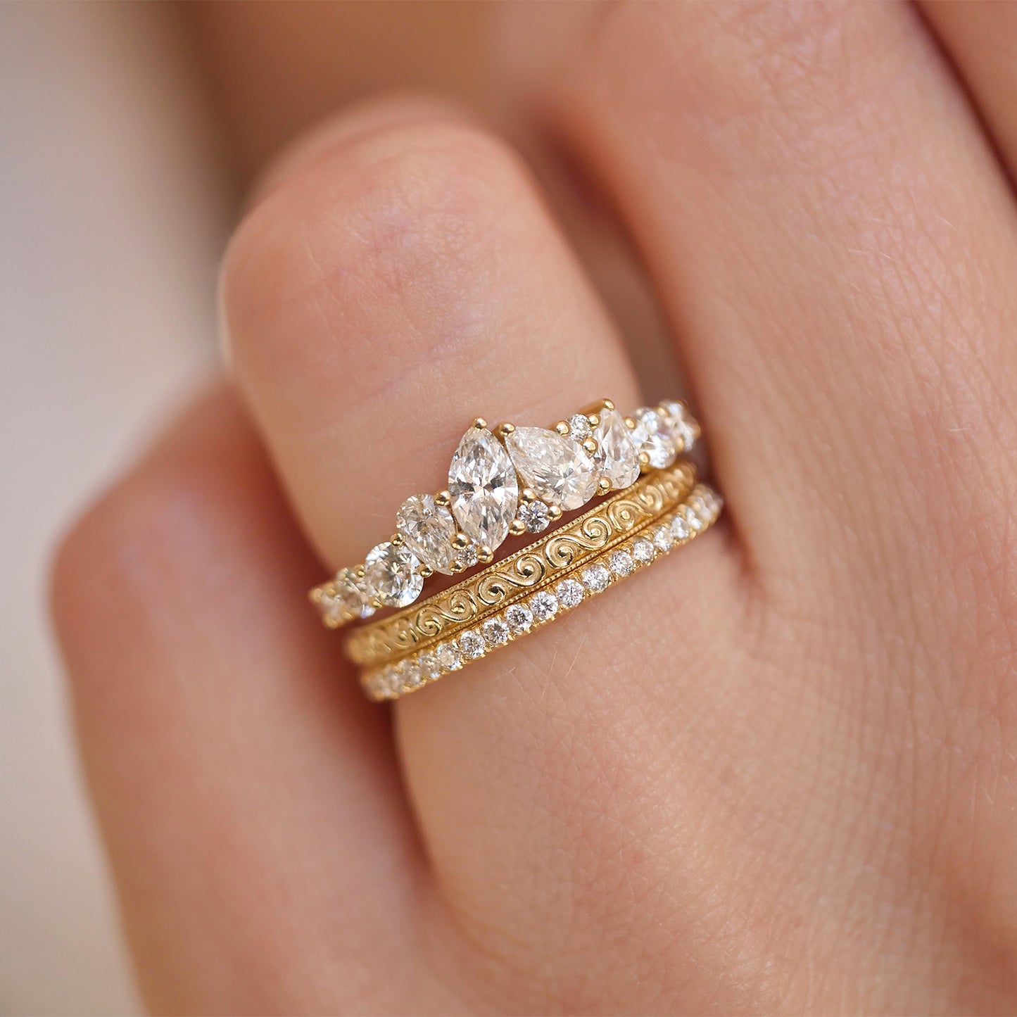 Woman wearing 14k yellow gold and diamond engagement ring with stacked wind spiral wedding band and pave diamond band.