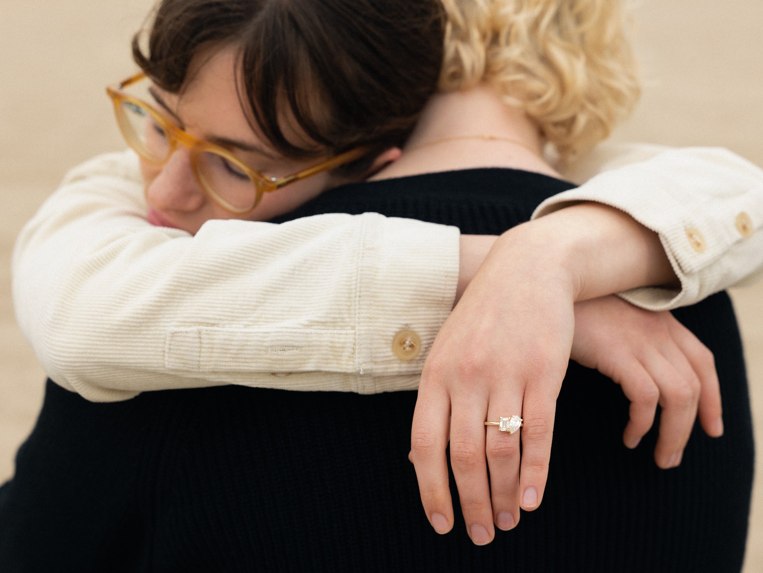 Couple hugging and woman wearing yellow gold emerald and pear shaped diamond toi et moi ring