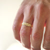 Man wearing 14k yellow gold wind-engraved wide wedding band.