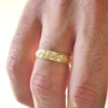 Close up of man wearing 14k yellow gold wind-engraved wedding band.