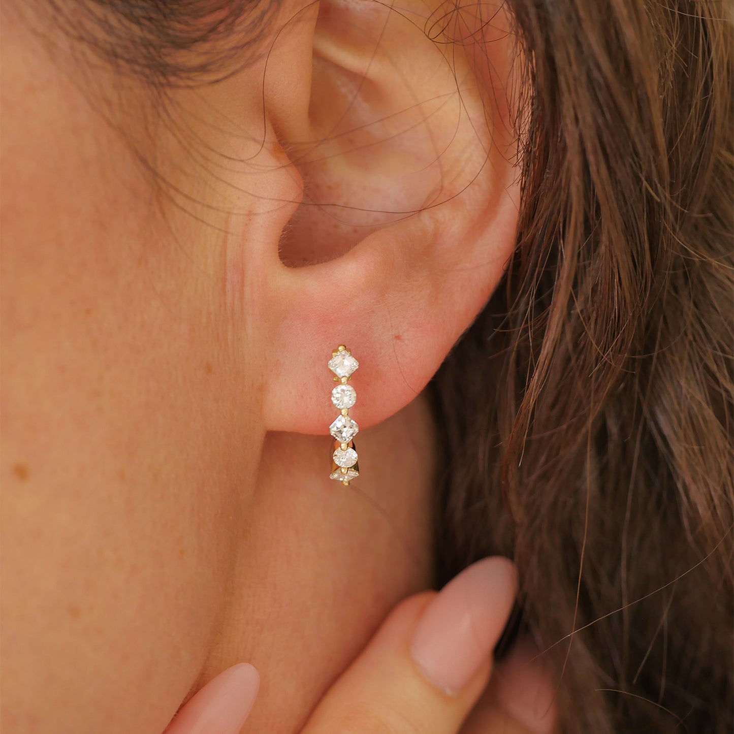 Woman wearing a pair of vintage diamond hoop earrings with six asscher cut diamonds and four round diamonds set in 18k yellow gold.