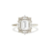 A white gold ring featuring a colorless emerald cut moissanite center stone with natural round brilliant diamonds around it.