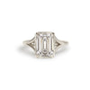 An emerald cut diamond solitaire ring with a white gold band and milgrain detailing.