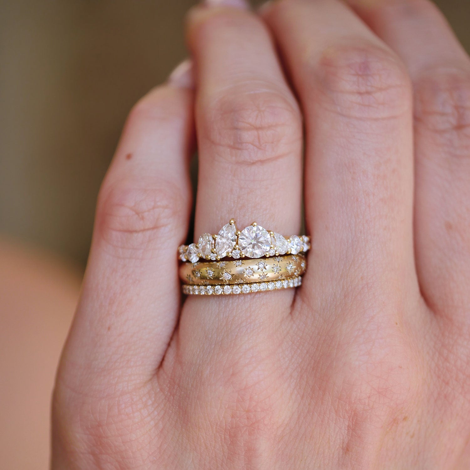 Hand wearing a diamond mosaic engagement ring, stacked with a star engraved and pave diamond band