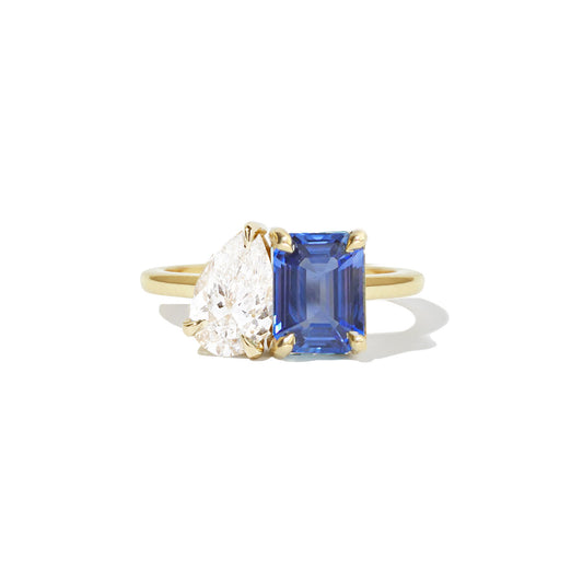 The ring elegantly combines a deep blue sapphire, a radiant green emerald, and a sparkling pear-shaped diamond, creating a truly unique and vibrant design.